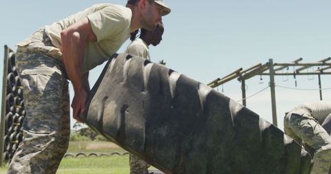 Diverse soldiers engaged in tire flipping on obstacle course