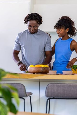 African american couple preparing meal on wooden kitchen island in bright minimalist home