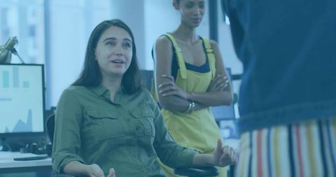 Woman gesturing during team discussion in modern open office with colleagues listening