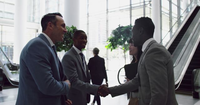 Business professionals greeting each other and shaking hands in modern office lobby. Ideal for depicting themes of collaboration, teamwork, corporate meetings, and networking in professional environments. Suitable for websites, presentations, and media focusing on business, professional relationships, and corporate culture.
