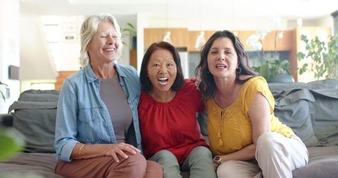 Multigenerational diverse women laughing together on gray sofa in bright open living area