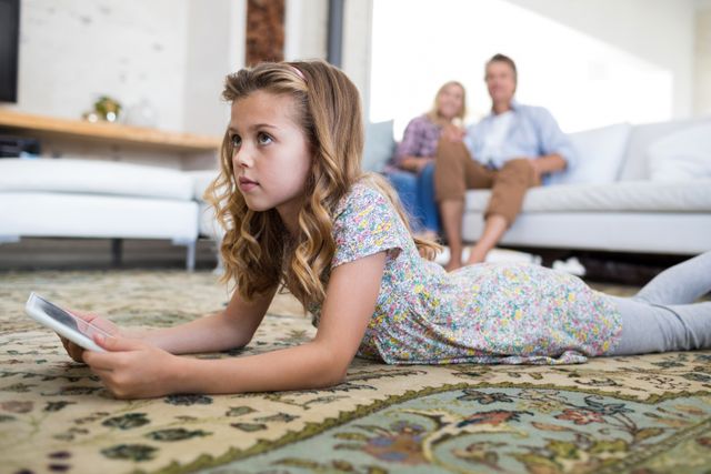 Daughter using digital tablet in living room while parents sitting on sofa at living room