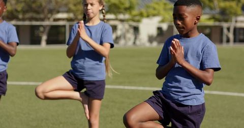 Elementary students practicing tree pose on school field — outdoor kids yoga and balance