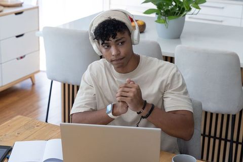 African american man wearing headphones and beanie working remotely at sunlit table