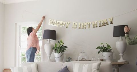 Two People Decorating Living Room with Birthday Banner
