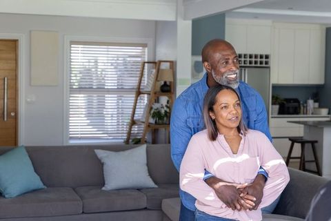 Black mature couple embracing and smiling in modern open-plan home near gray sofa