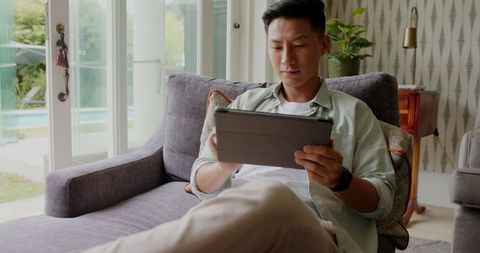 Man Relaxed on Sofa Using Tablet Device Near Large Window Light