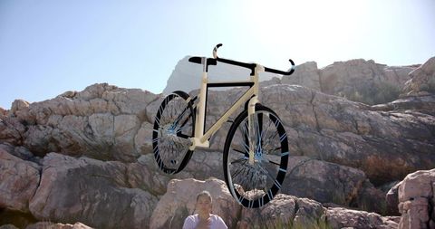 Hovering beige bicycle over rocky outcrop backlit by sun, woman checking phone