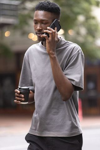 African man walking while talking on smartphone holding takeaway coffee cup urban lifestyle
