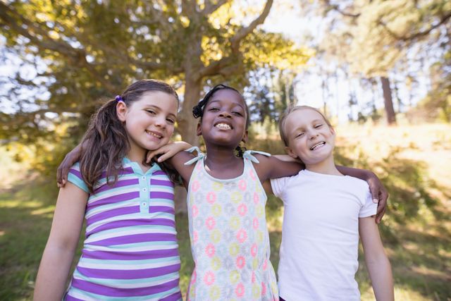 Three young girls standing close together in a forest, smiling and enjoying a sunny day. Ideal for use in advertisements, educational materials, and articles about childhood, friendship, and outdoor activities. Perfect for promoting diversity, happiness, and the joys of spending time in nature.