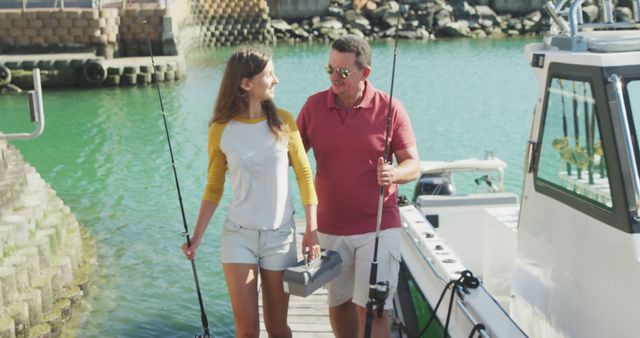 Happy caucasian father and teenage daughter walking on jetty with fishing rods and tackle box. Leisure, free time, hobbies, family, travel and vacations.