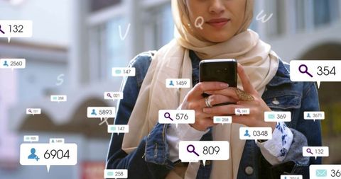 Young woman wearing headscarf tapping smartphone with floating social media notifications