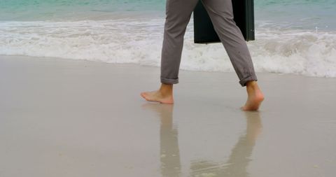 Businessman walking on beach holding briefcase, barefoot reflection