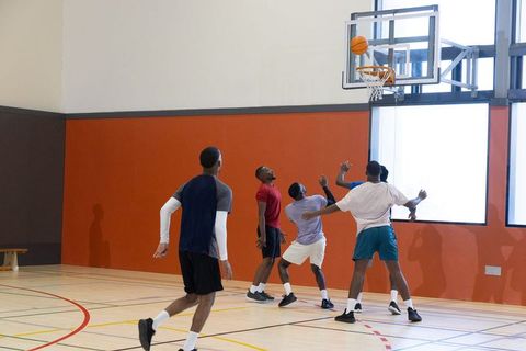 Diverse men playing pickup basketball indoors near rim on hardwood court