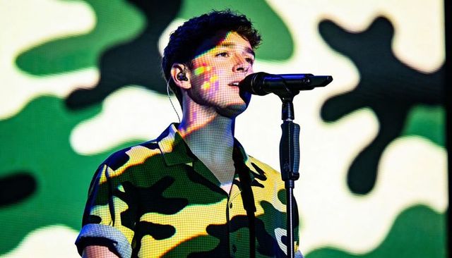 Singer performing in camo shirt with led camouflage backdrop and microphone on stage