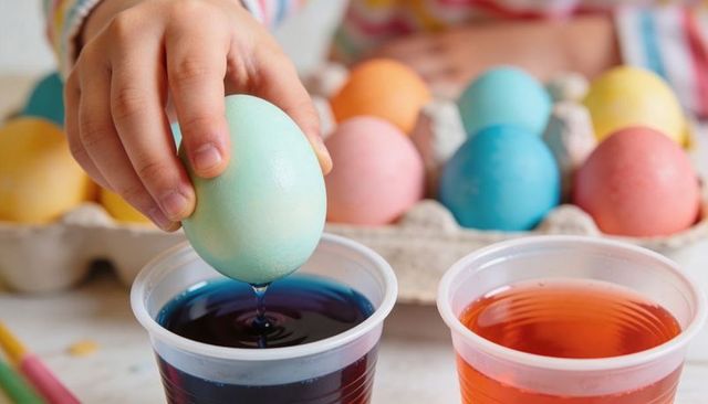 Child dipping pastel easter egg into dye cups, hand dripping violet dye closeup