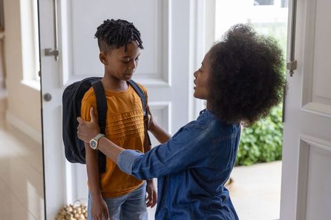 African american mother adjusting backpack for son at front door morning school sendoff