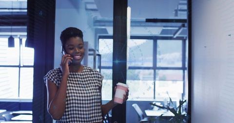 Businesswoman Holding Coffee and Talking on Smartphone in Office Environment
