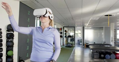 Woman Training with VR Headset in Gym Reaching for Virtual Exercise and Rehabilitation