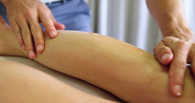 Physical therapist's hands performing massage on patient's calf muscle in a clinic. Ideal for articles and marketing materials related to physical therapy, rehabilitation, wellness treatments, and healthcare services. This close-up can also be used in brochures, websites, and visual aids for clinics promoting their massage and manual therapy services.