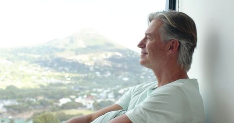 Mature man gazing through window over sunlit valley, peaceful reflective moment
