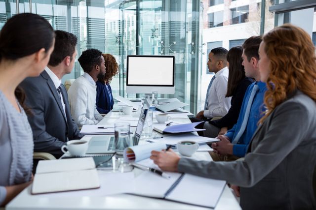 Business professionals are engaged in a video conference in a modern office. Ideal for illustrating teamwork, corporate meetings, and technological collaboration. Suitable for content related to business strategy, remote work, professional discussions, and office environments.