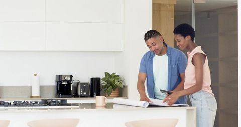 Couple planning stylish kitchen renovation with blueprints and tablet in modern home