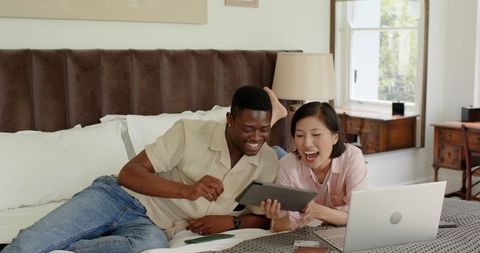 Diverse couple shopping online together in cozy bedroom