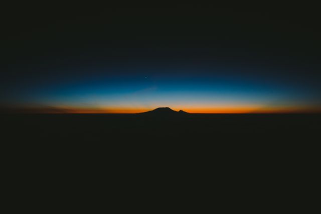 Beautiful scene of a sunrise over a distant mountain range highlighting a colorful horizon that transitions from dark night sky to dawn. Ideal for backgrounds, nature-related content, travel publications, and screensavers. Conveys themes of tranquility, peace, and the start of a new day.