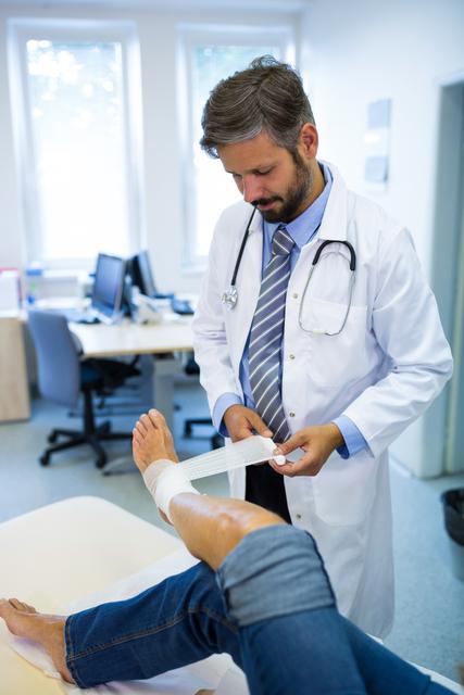 Male doctor bandaging foot of female patient in hospital room. Ideal for use in healthcare, medical care, and injury treatment contexts. Useful for illustrating medical procedures, patient care, and professional healthcare services.