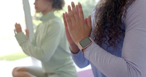 Practicing mindful yoga with smartwatch-wearing woman in lavender top pressing palms