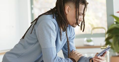 Mid-adult African American man checking smartphone at kitchen counter in light blue sweatshirt