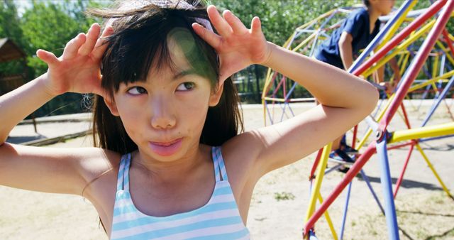 Girl playing in playground, making funny faces, enjoying summer day. Suitable for topics on childhood, outdoor fun, playtime, and kid’s activities.