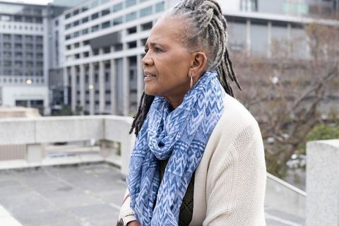 Contemplative african american senior woman leaning on rooftop parapet with urban skyline wearing sc