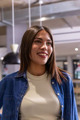 Young woman smiling in modern coworking space wearing denim shirt and cream top