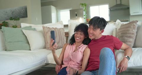 Young couple taking selfie on cozy living room couch smiling and relaxing together