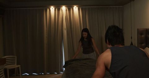Couple making bed at night cozy bedroom scene with dim lighting and heavy curtains