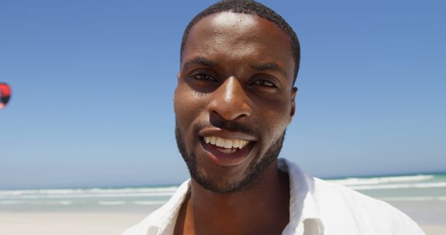 A cheerful African American man enjoys a sunny day at the beach, with copy space. His bright smile and casual attire suggest a relaxed and happy mood in the outdoor setting.