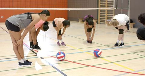 Diverse female volleyball team warming up and stretching on indoor gym court