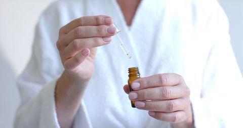 Mature woman applying skincare serum with dropper bottle at home