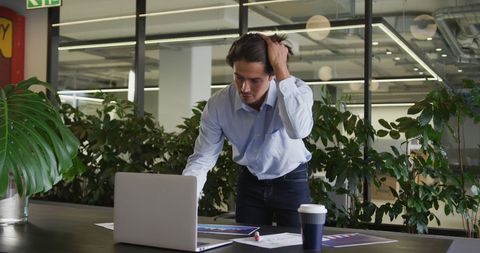 Focused Businessman using Laptop reviewing paperwork at Modern Office - Download Free Stock Images Pikwizard.com