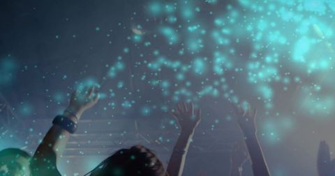 Nightclub crowd reaching toward teal stage lights, haze and wristbands creating energetic nightlife