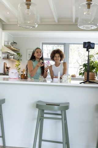 African american women filming skincare tutorial in bright modern kitchen with smartphone