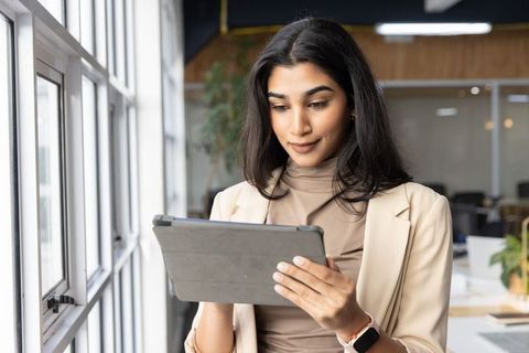 Indian businesswoman using tablet near window in modern office, focused professional