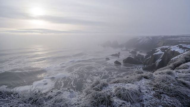 Misty frosted coastal cliffs at sunrise with swirling sea foam and rocky headlands, winter