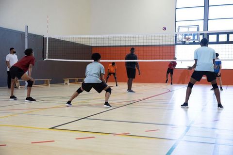 African american men playing indoor volleyball team defending and spiking on gym court
