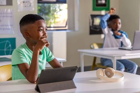 African american boys using tablet and laptop in classroom learning with headphones