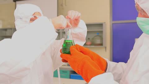 Scientists Analyzing Green Liquid in Laboratory Safety Suits