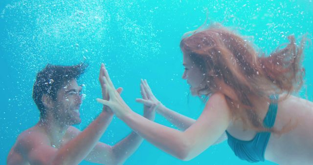 A cheerful couple swimming underwater, touching hands and smiling, creating a playful, intimate moment. Useful for vacation promotions, leisure activities, relationship and bonding themed content, and lifestyle blogs.