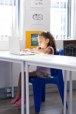 Young girl using laptop in bright classroom studying and focusing on remote learning